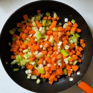 Diced carrots, onion, and celery sautéing in a skillet ; flavor base for chicken pot pie casserole filling.