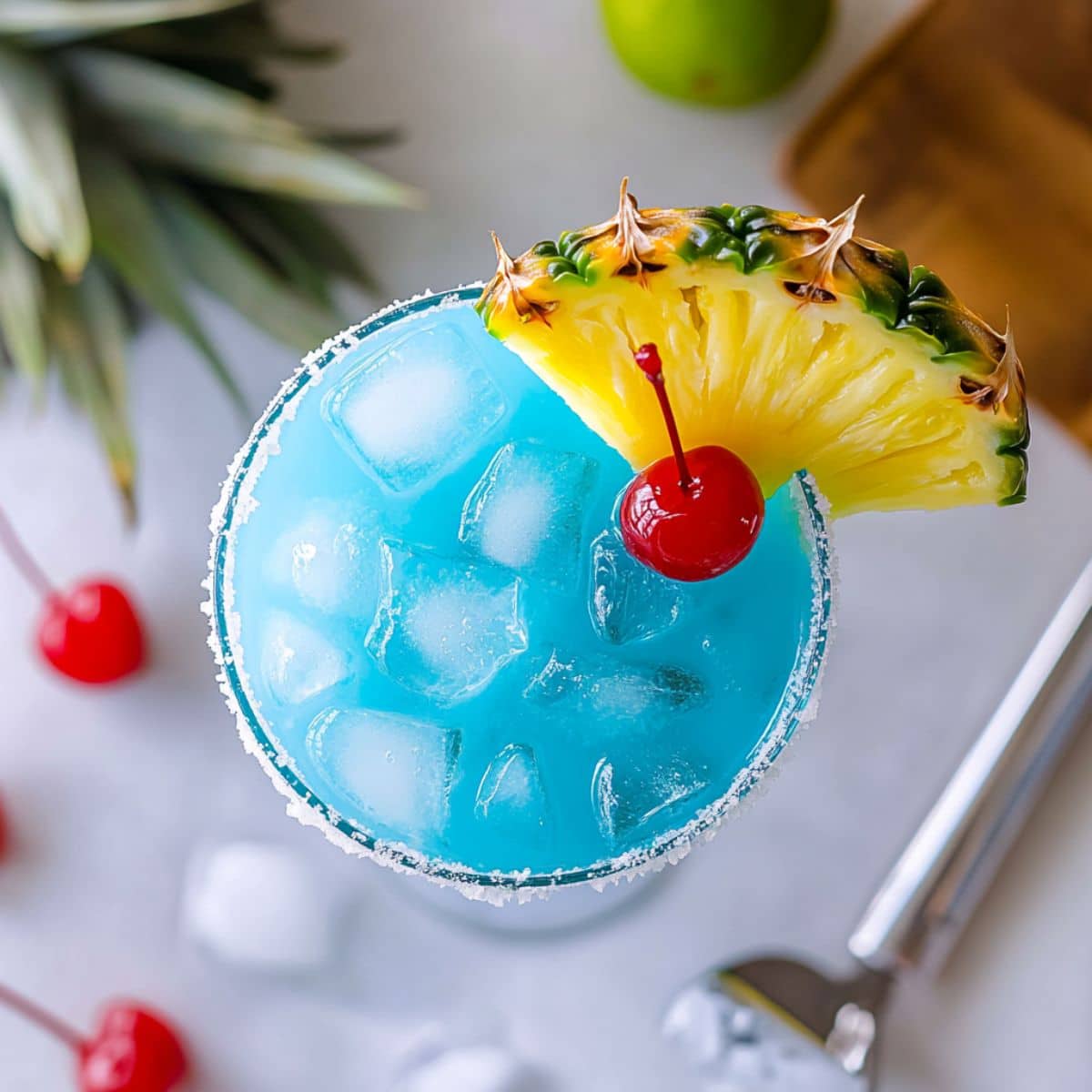 Garnished Blue Hawaiian Margarita with pineapple and lime, ready to serve on white kitchen counter.