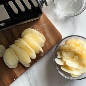 Thinly sliced russet potatoes on a cutting board, ready for layering in au gratin potatoes