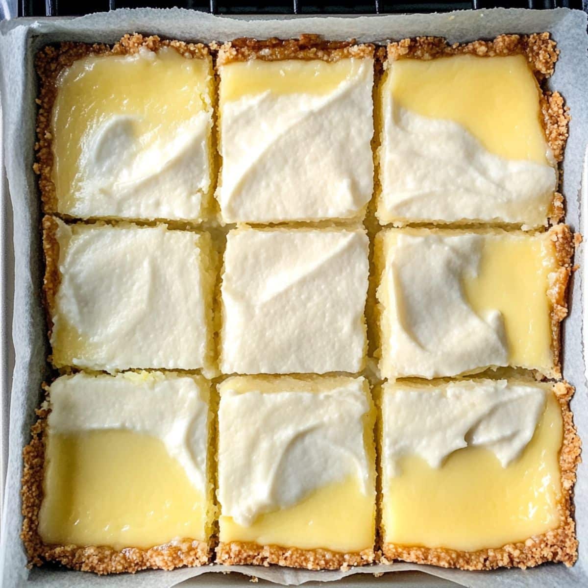 Key lime bars baking in an oven with a barely set center. Edges golden and parchment visible.