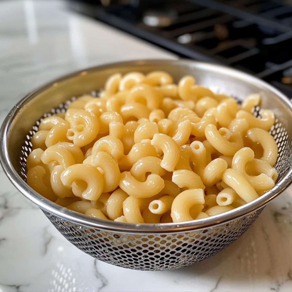 Soft elbow macaroni draining in a white colander after boiling. Cooled and ready to soak up dressing for creamy Hawaiian mac salad.