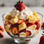 Homemade strawberry shortcake trifle in a glass bowl with whipped cream, fresh strawberries, and pound cake cubes. Rustic, layered, and ready to serve.