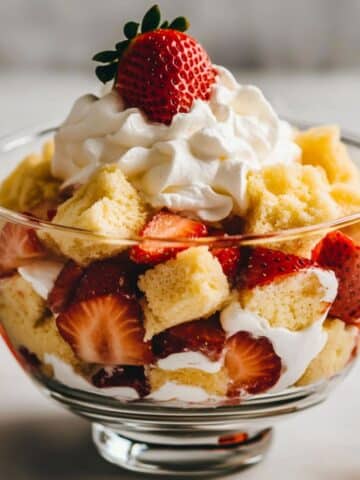Homemade strawberry shortcake trifle in a glass bowl with whipped cream, fresh strawberries, and pound cake cubes. Rustic, layered, and ready to serve.