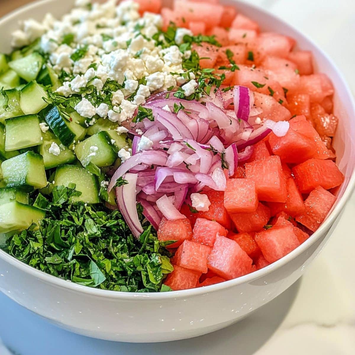 Assembled watermelon cucumber salad with feta, mint, and red onion in a white bowl. Juicy and casually tossed for homemade freshness.