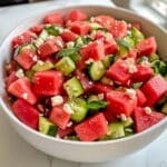 Juicy watermelon cucumber salad with feta and mint, fully mixed in a white bowl on marble. Fresh, vibrant, and homemade for summer.