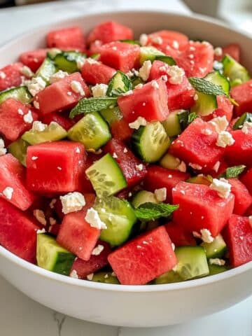 Juicy watermelon cucumber salad with feta and mint, fully mixed in a white bowl on marble. Fresh, vibrant, and homemade for summer.