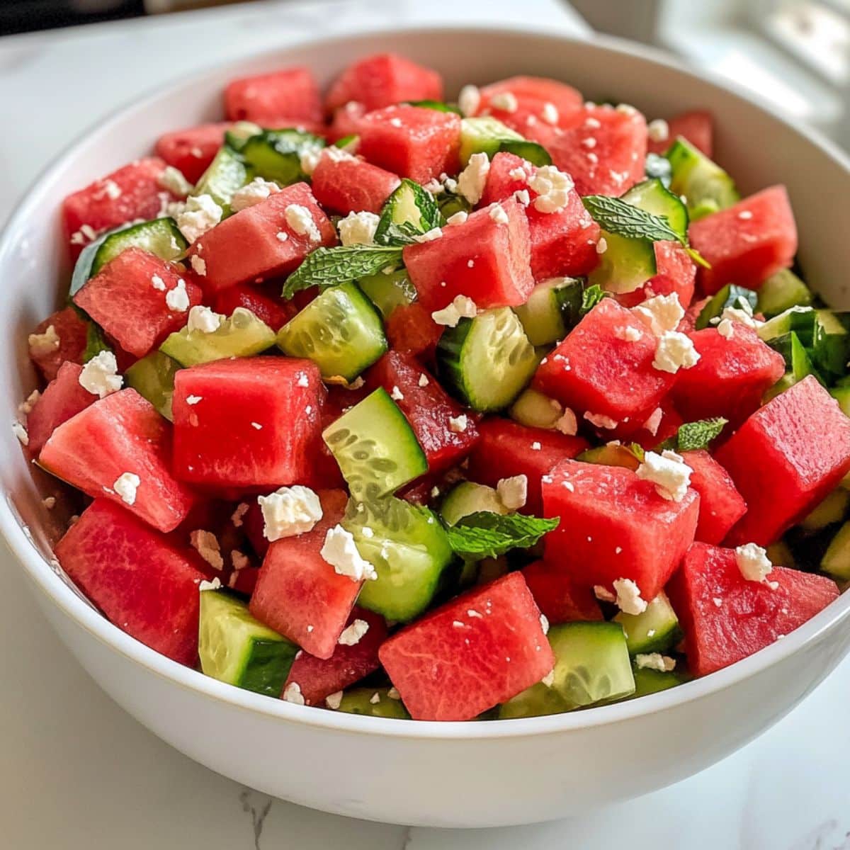 Juicy watermelon cucumber salad with feta and mint, fully mixed in a white bowl on marble. Fresh, vibrant, and homemade for summer.