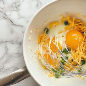 Whisked eggs with veggies and cheese in a mixing bowl, ready to bake into a fluffy frittata.