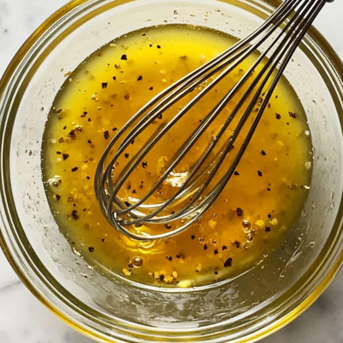 Simple vinaigrette being whisked in a mason jar with visible oil and vinegar.