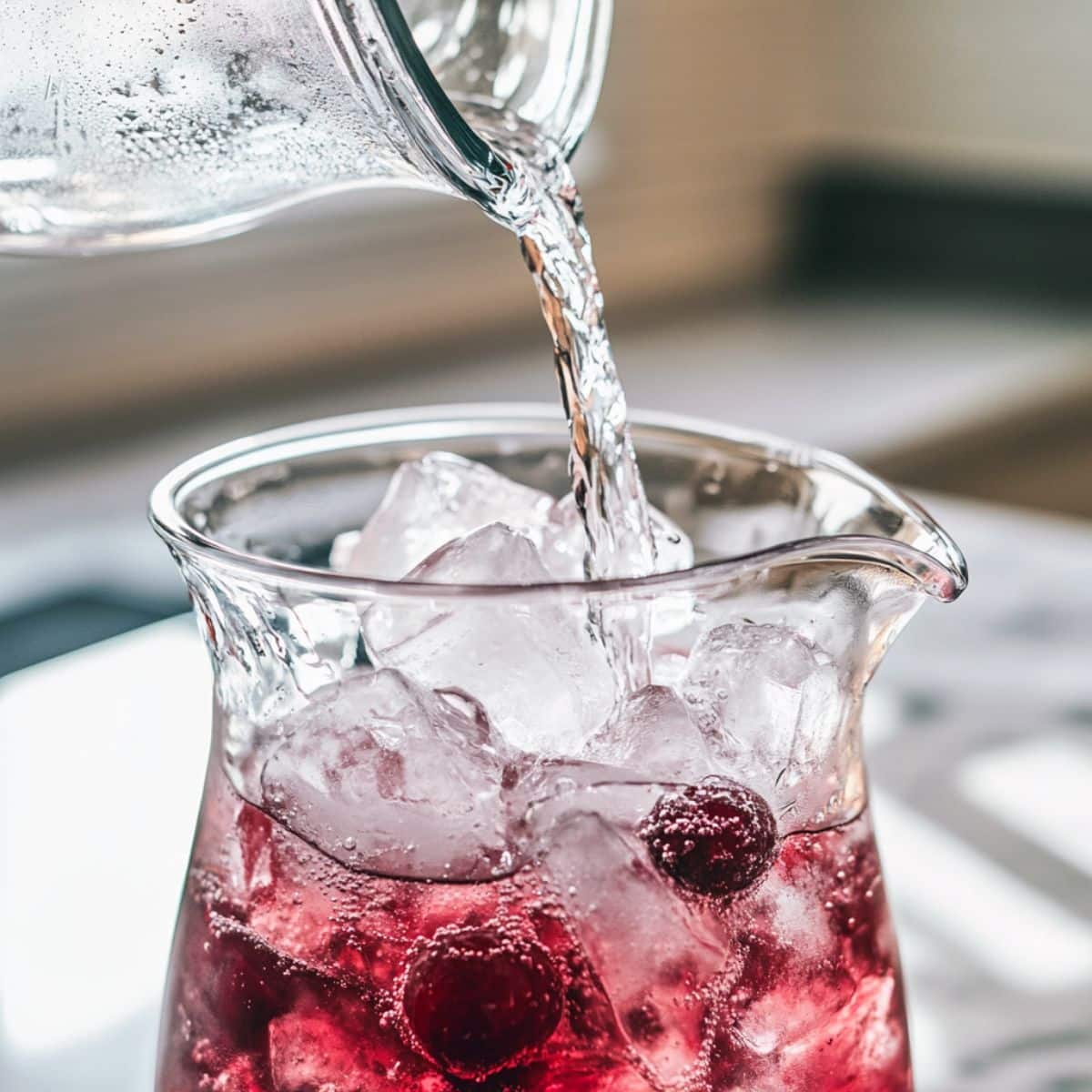 Sparkling water added to cherry limeade mix with visible fizz. Homemade version on white kitchen counter.