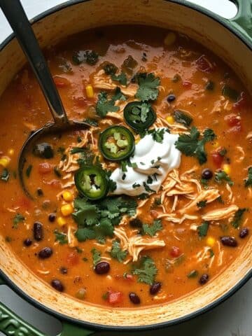 Overhead view of creamy chicken enchilada soup in a bowl with toppings. Homemade style shot on a white kitchen counter.