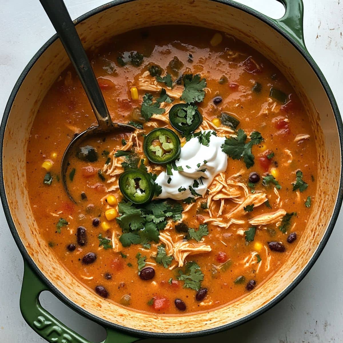 Overhead view of creamy chicken enchilada soup in a bowl with toppings. Homemade style shot on a white kitchen counter.