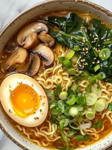 Close-up of steaming homemade ramen noodles on white marble counter. Soft egg, rich broth.