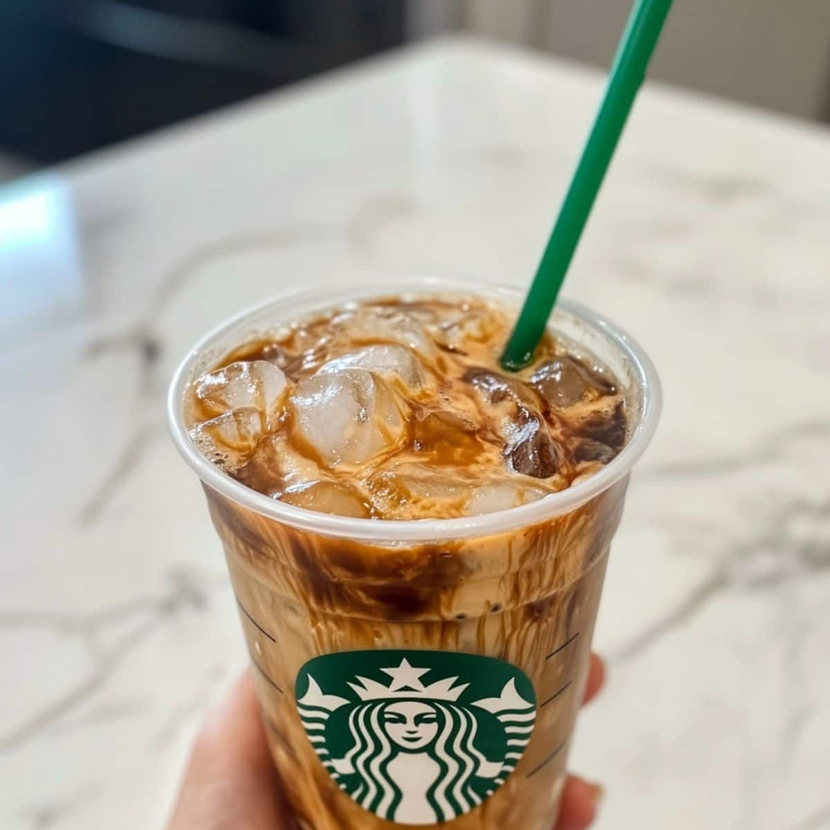 Starbucks iced coffee in a plastic cup with creamy swirls and ice cubes. A homemade copycat drink that looks refreshingly café-ready.