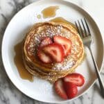 Stack of fluffy almond flour pancakes topped with butter and syrup. Homemade weekend breakfast on white counter.