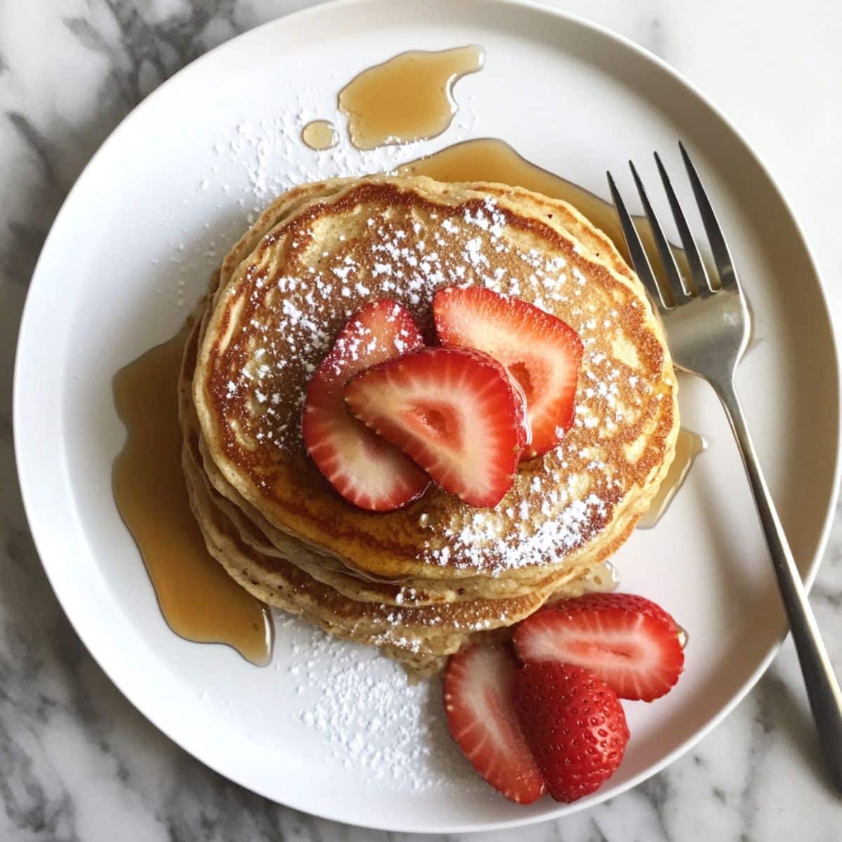 Stack of fluffy almond flour pancakes topped with butter and syrup. Homemade weekend breakfast on white counter.