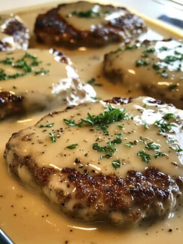 Creamy amish hamburger steak bake casserole with juicy beef patties smothered in thick white gravy. Real homemade look from an overhead kitchen shot.