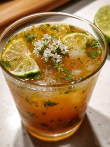 Homemade apple cider vinegar drink with crushed ice, lime slices, and mint on a white counter. Real kitchen feel, fresh and natural morning tonic.