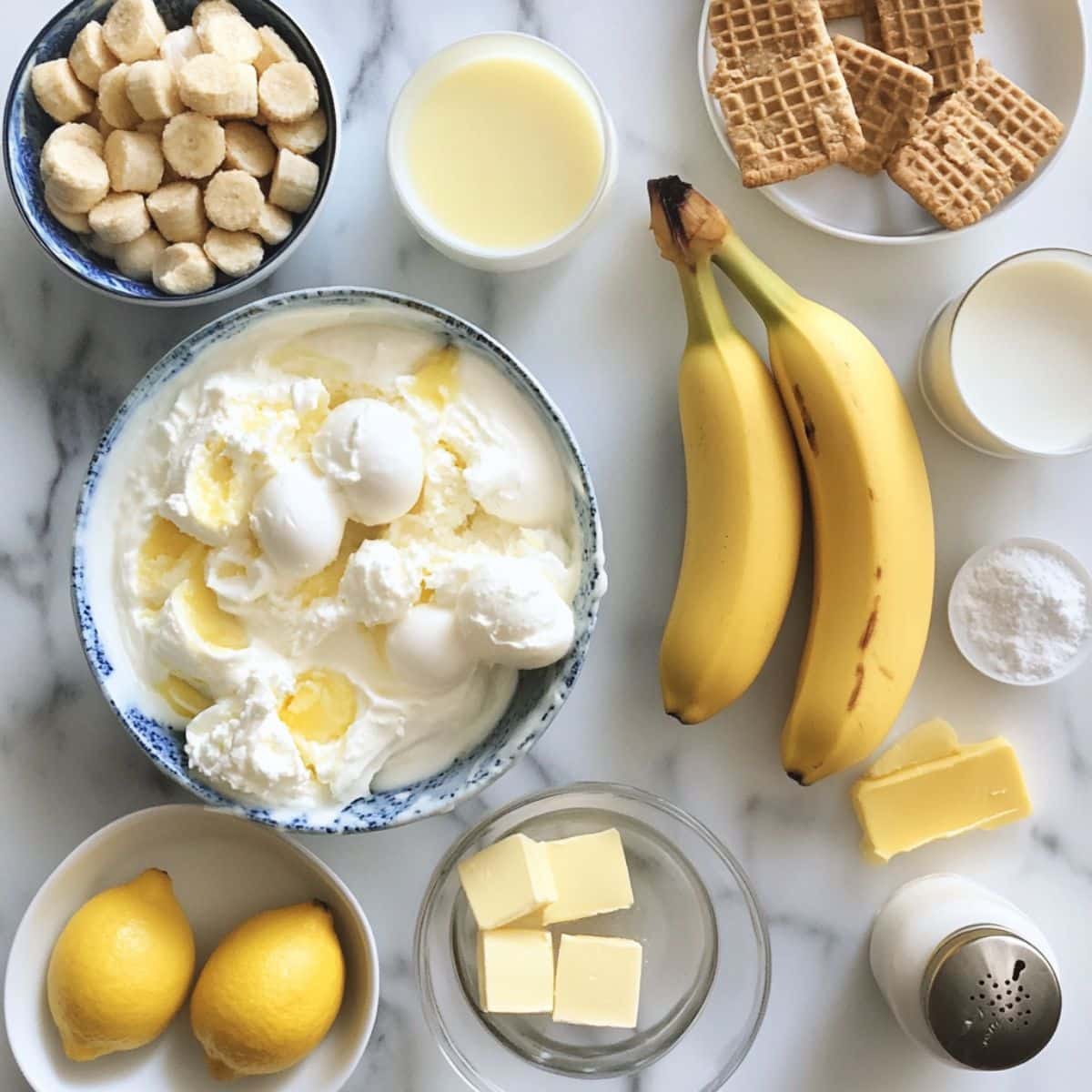 banana pudding ice cream ingredients laid out on a white kitchen counter. Ripe bananas, Nilla wafers, vanilla, and cream in real kitchen prep.