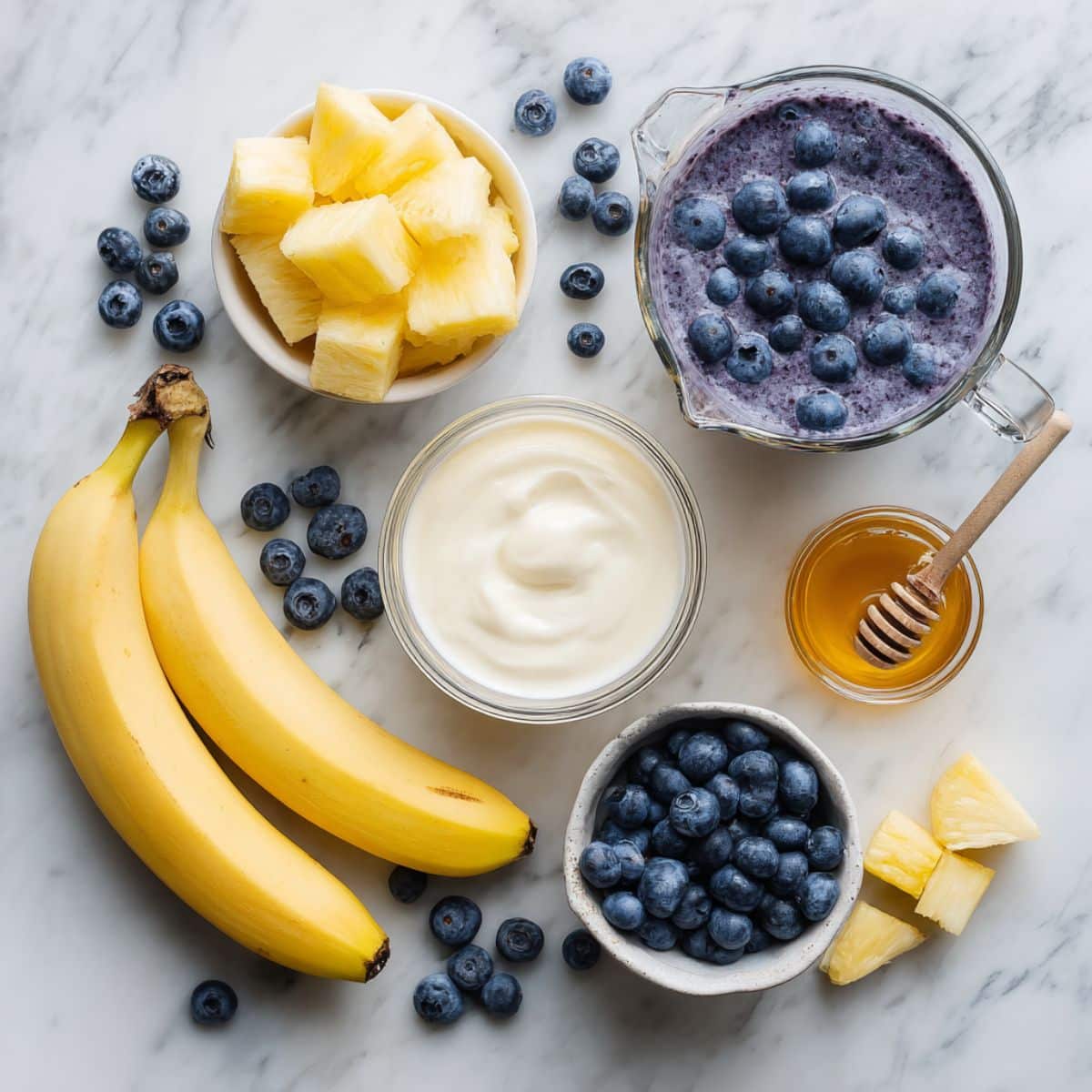 Frozen and fresh blueberry smoothie ingredients including blueberries, banana, pineapple chunks, Greek yogurt and other ingredients.