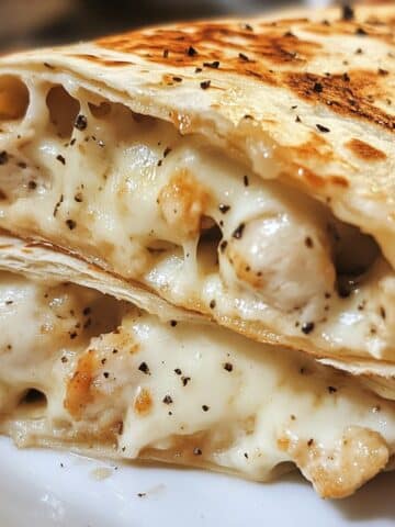 Melted cheesy garlic chicken wraps cut open and stacked, filled with creamy chicken and black pepper. Golden crispy tortillas shine with garlic butter.