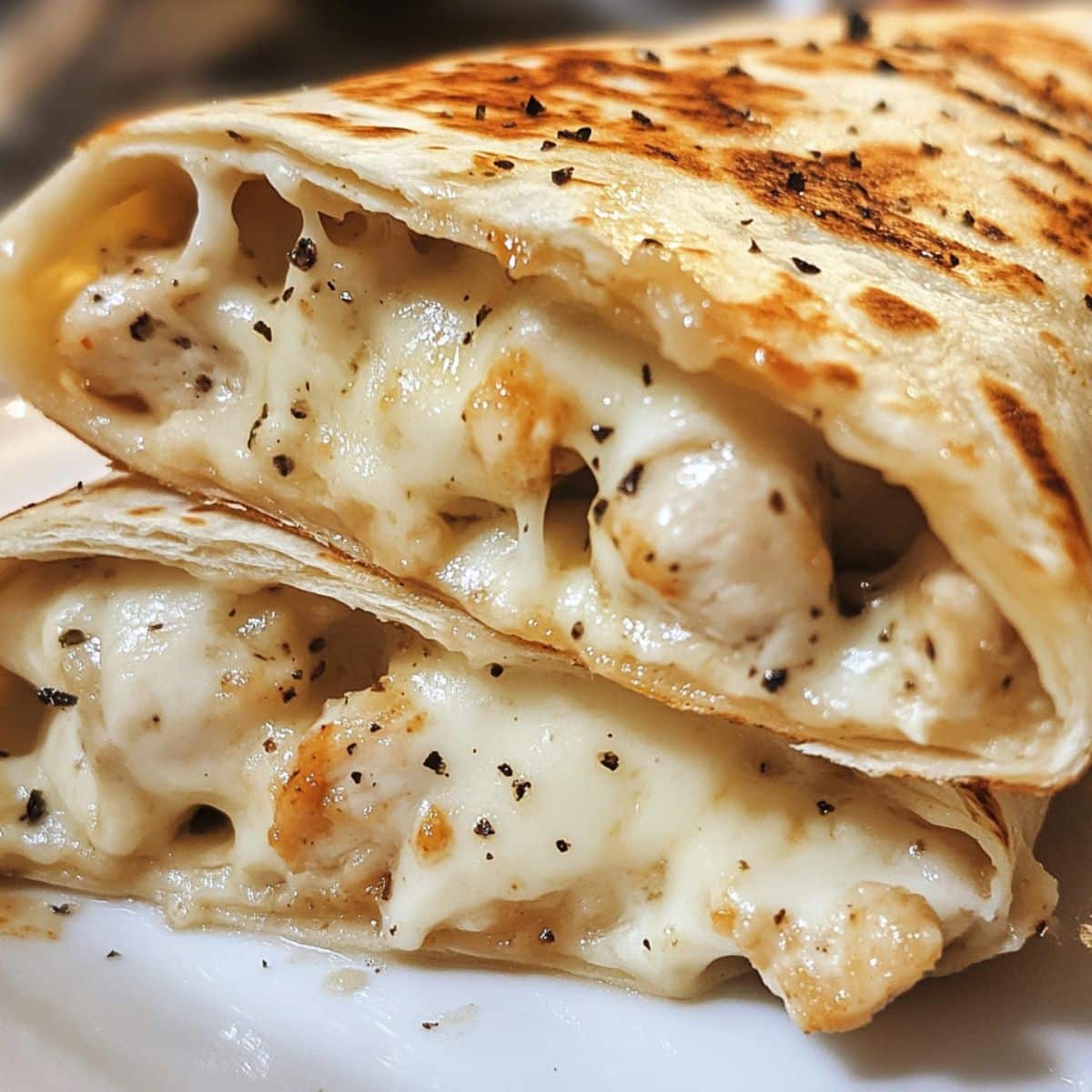 Melted cheesy garlic chicken wraps cut open and stacked, filled with creamy chicken and black pepper. Golden crispy tortillas shine with garlic butter.