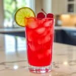 Glass of cherry limeade with lime and cherry on white kitchen counter. Real fruit drink made fresh at home.