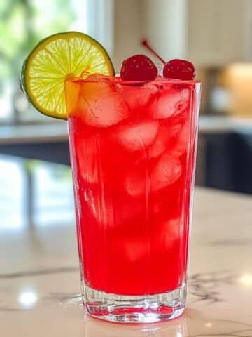 Glass of cherry limeade with lime and cherry on white kitchen counter. Real fruit drink made fresh at home.