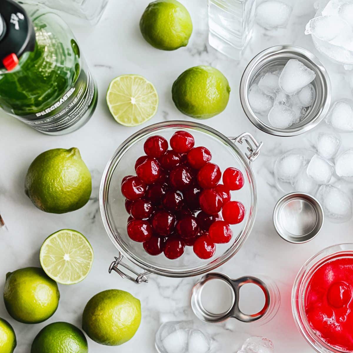 Cherry limeade ingredients including limes, cherries with syrup, and sparkling water on a white kitchen counter.