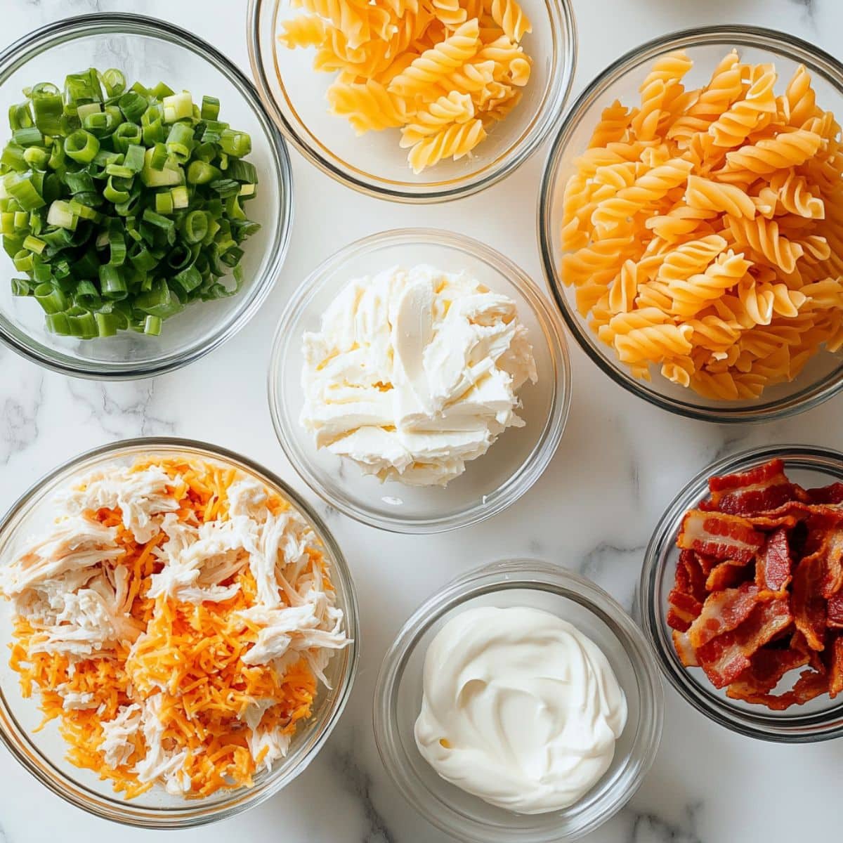 All ingredients for chicken bacon ranch casserole laid out on a white kitchen counter. Includes pasta, bacon, chicken, cheese, and ranch mix.