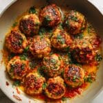 Close-up of golden chicken meatballs in bubbling marinara sauce with parsley.