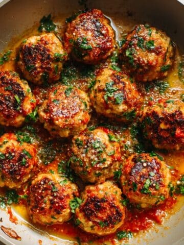 Close-up of golden chicken meatballs in bubbling marinara sauce with parsley.