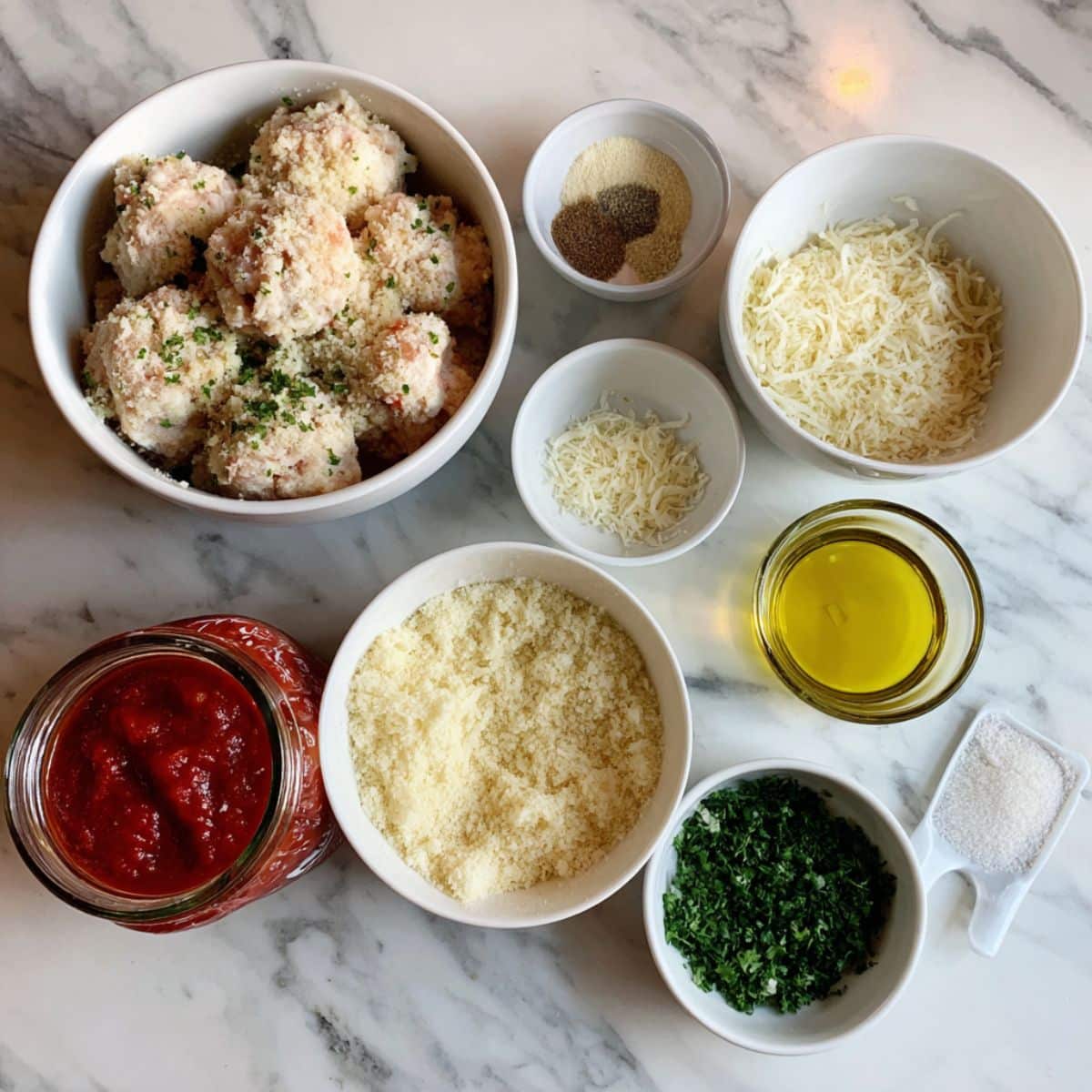 chicken meatball ingredients laid out on a white kitchen counter. Includes ground chicken, breadcrumbs, herbs, and marinara sauce.
