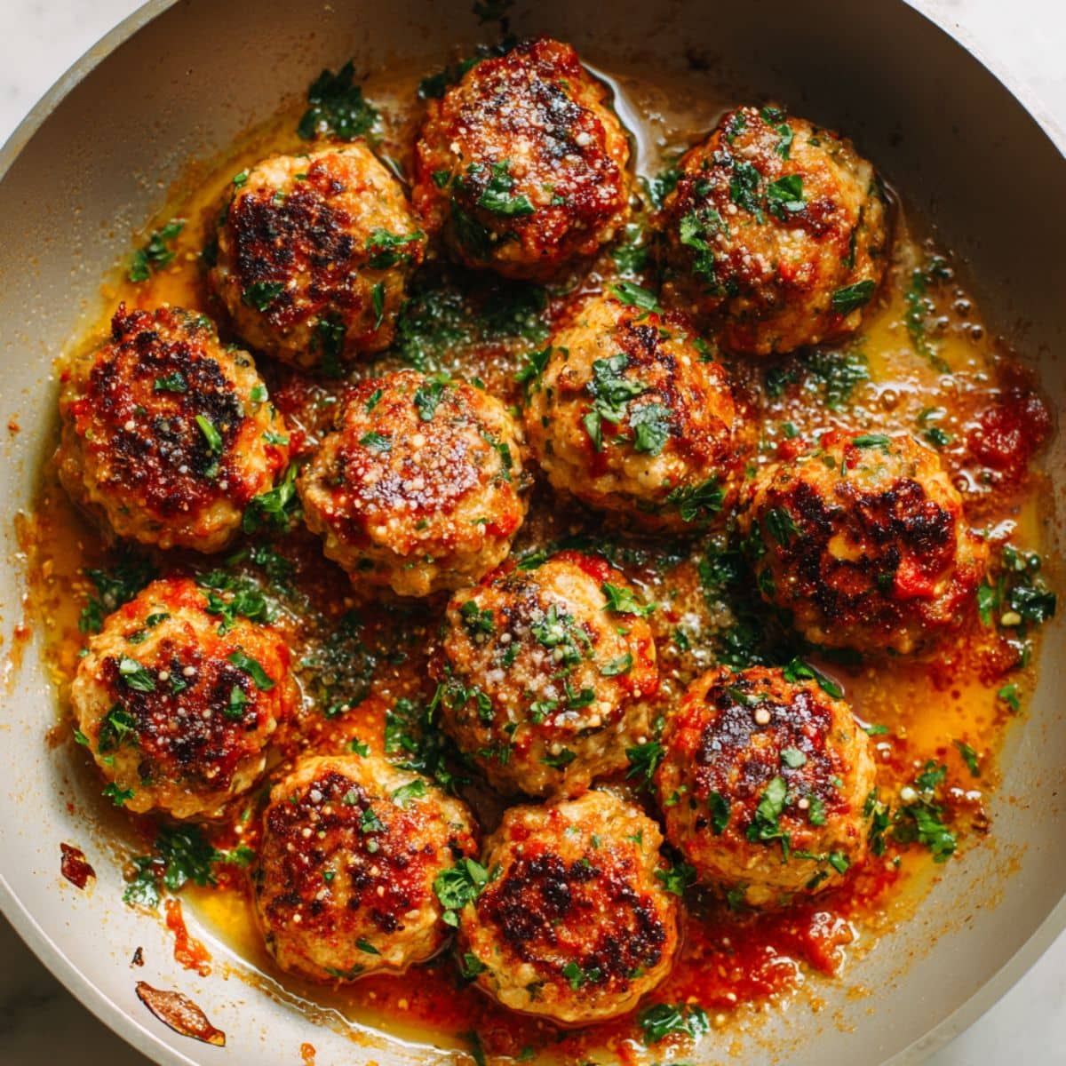 Close-up of golden chicken meatballs in bubbling marinara sauce with parsley.