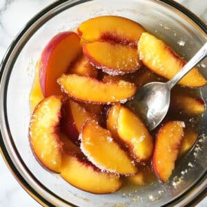 Fresh peach slices in sugar and lemon juice macerating in a mixing bowl. Prepped for trifle layering.