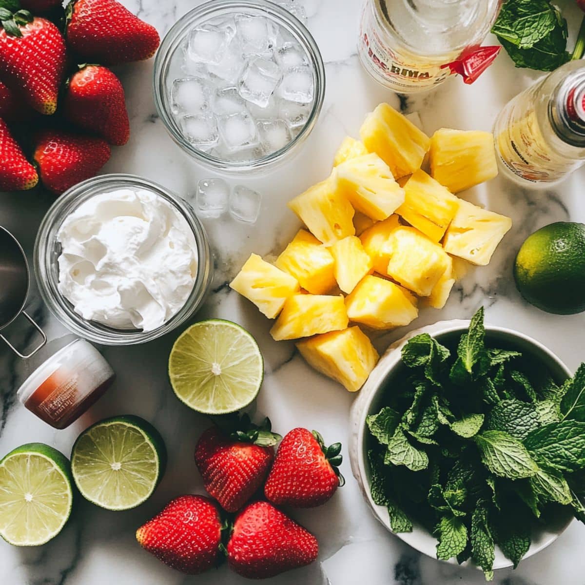 All ingredients for homemade strawberry piña colada on white counter. Includes fruit, coconut cream, rum, and lime.