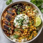 Homemade street corn chicken rice bowl with juicy grilled chicken, corn, beans, rice, and crema in white bowl.
