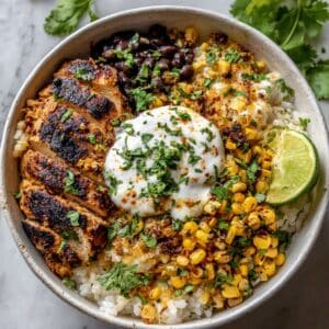 Homemade street corn chicken rice bowl with juicy grilled chicken, corn, beans, rice, and crema in white bowl.