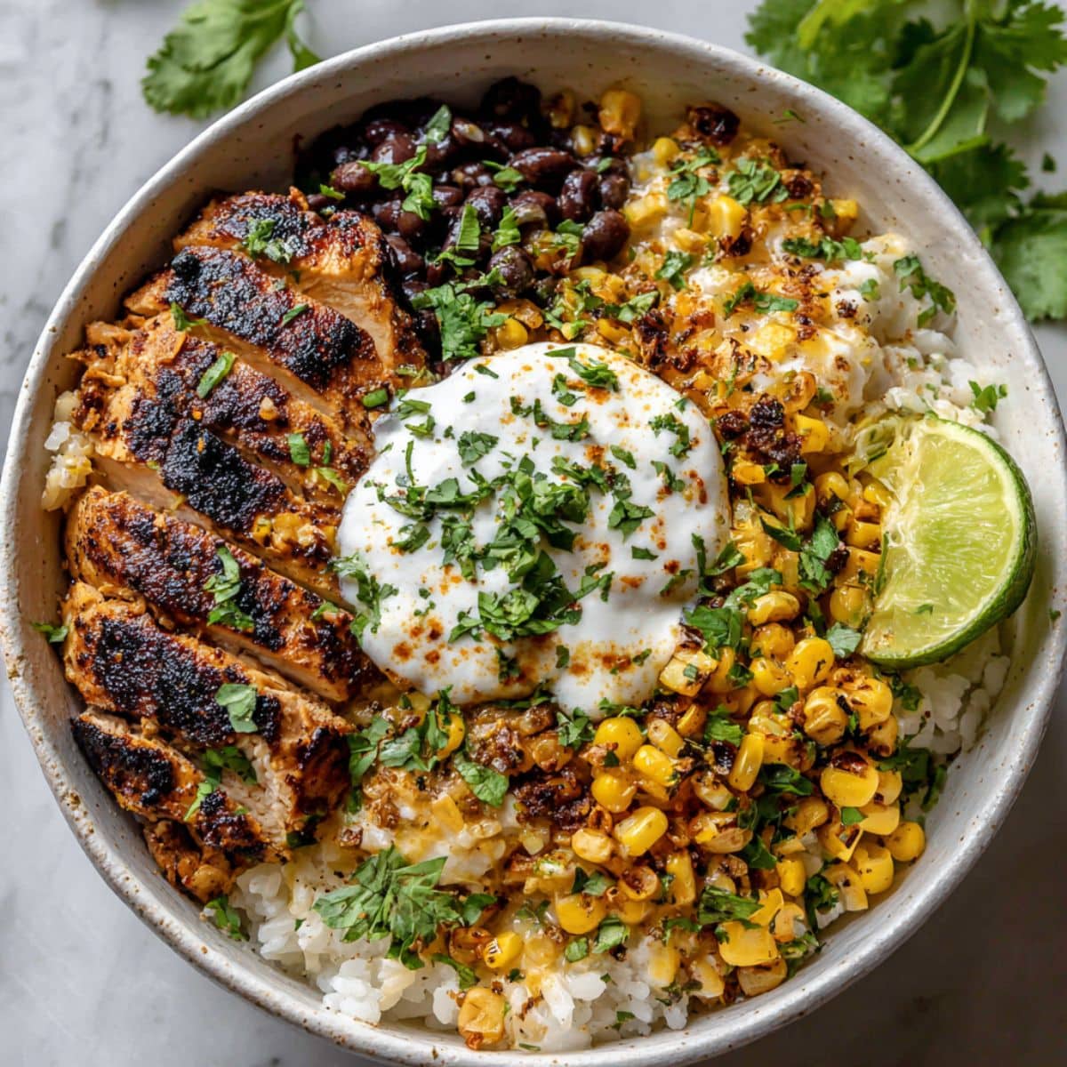 Homemade street corn chicken rice bowl with juicy grilled chicken, corn, beans, rice, and crema in white bowl.