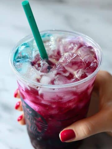 Homemade Summer Berry Refresher Starbucks copycat with ombré magenta-to-blue layers, ice cubes, and teal straw on white marble.