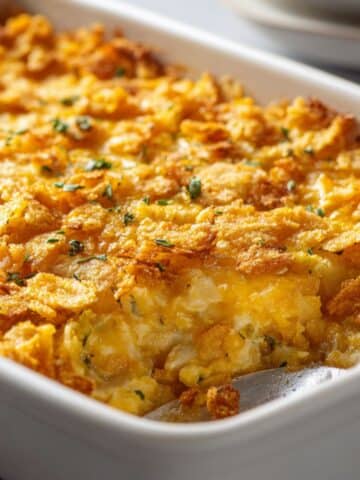 Homemade yellow squash casserole with golden cheese and cracker topping in baking dish.