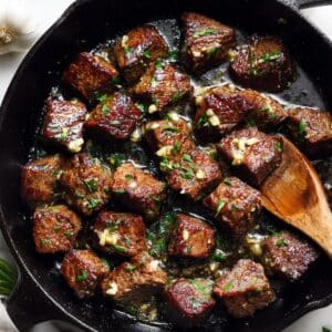 Golden seared garlic butter steak bites in cast iron skillet with melted butter and fresh herbs.