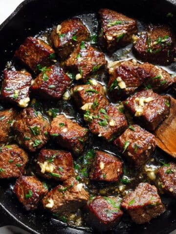Golden seared garlic butter steak bites in cast iron skillet with melted butter and fresh herbs.