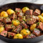 Juicy garlic butter steak bites and golden potatoes freshly cooked in a cast iron skillet, glistening with melted butter, chopped parsley, and seared to tender perfection for a hearty homemade dinner.