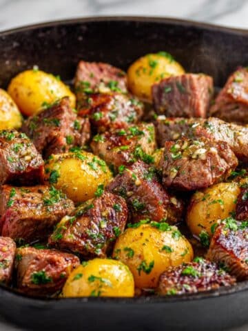 Juicy garlic butter steak bites and golden potatoes freshly cooked in a cast iron skillet, glistening with melted butter, chopped parsley, and seared to tender perfection for a hearty homemade dinner.