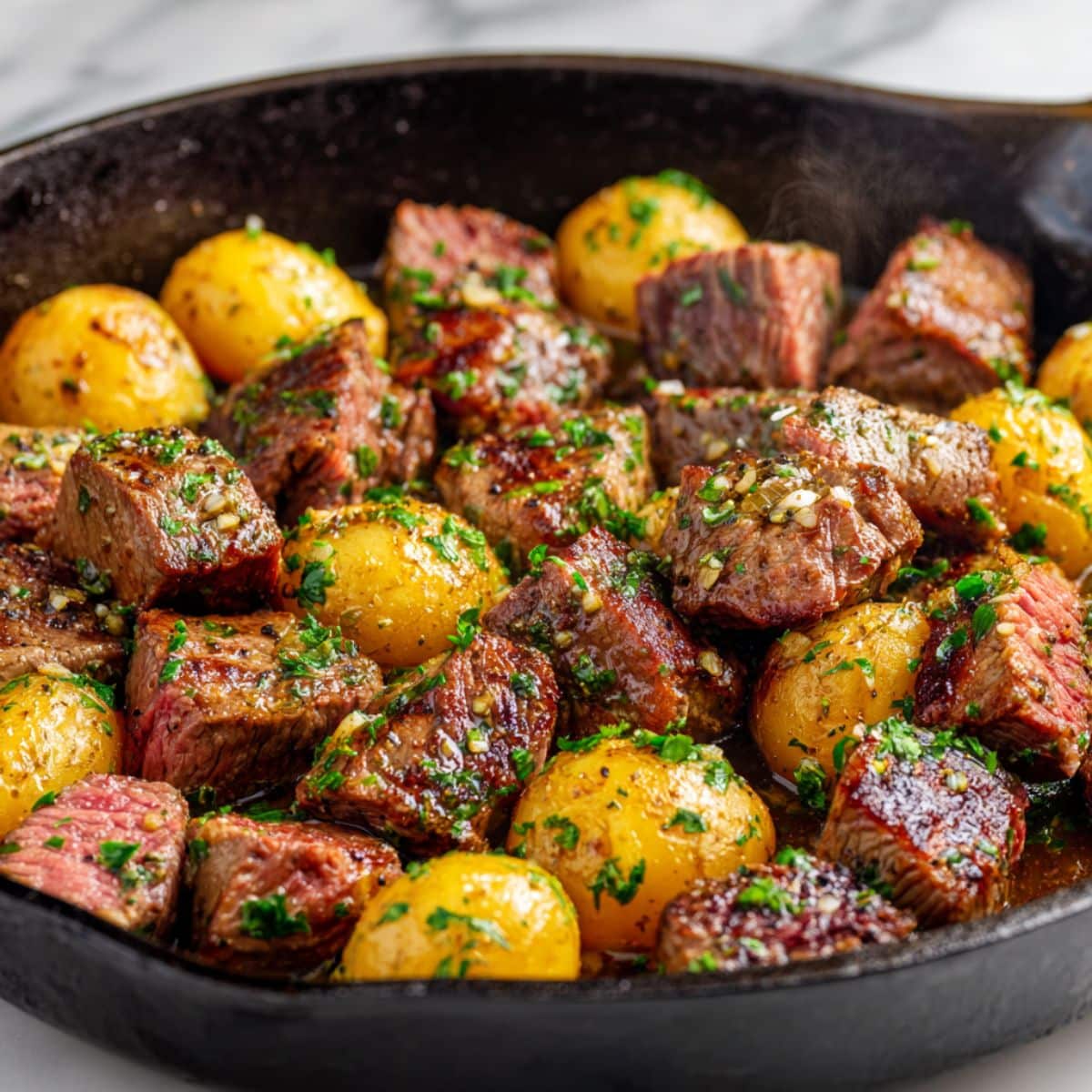 Juicy garlic butter steak bites and golden potatoes freshly cooked in a cast iron skillet, glistening with melted butter, chopped parsley, and seared to tender perfection for a hearty homemade dinner.