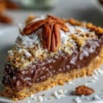 Slice of no-bake German chocolate pie with fudgy chocolate filling and gooey coconut pecan topping. Golden graham crust and homemade texture on white plate.