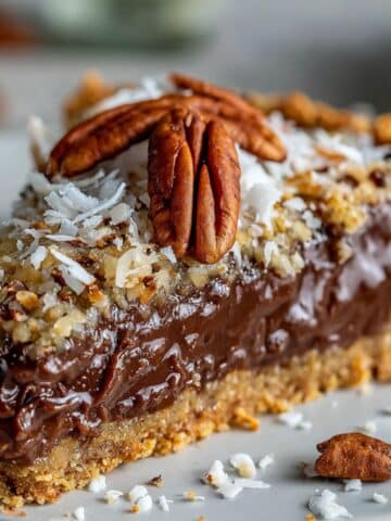 Slice of no-bake German chocolate pie with fudgy chocolate filling and gooey coconut pecan topping. Golden graham crust and homemade texture on white plate.