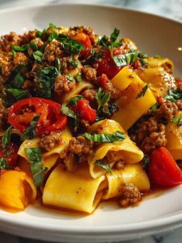 Italian drunken noodles with wide pasta ribbons, spicy sausage, cherry tomatoes, and fresh basil in a rich garlic-wine sauce.