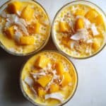 Homemade mango sago recipe in clear bowls showing creamy orange dessert with tapioca pearls. Asian tropical dessert with fresh mango chunks and coconut milk on kitchen counter.